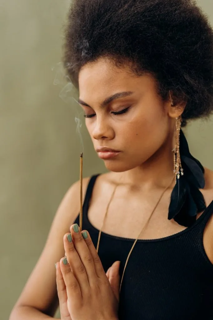 a-woman-doing-ritual-6931887 Woman meditating with closed eyes and incense, highlighting spiritual tranquility.